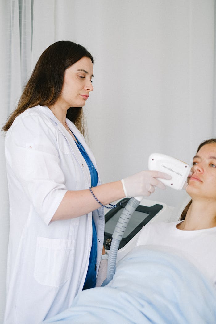 Side view of calm cosmetologist in medical uniform touching face of woman client with probe while doing low level laser therapy