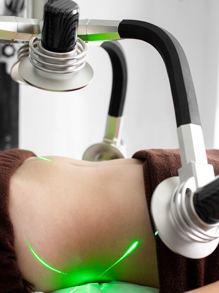 Services Crop faceless female client lying under modern laser weight loss machine with heads during treatment in modern light medical clinic